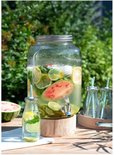 Glazen drankdispenser in de tuin, gevuld met water, citroen, limoen, kiwi en watermeloen, met kleine flesjes.