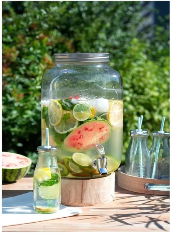 Glazen drankdispenser in de tuin, gevuld met water, citroen, limoen, kiwi en watermeloen, met kleine flesjes.