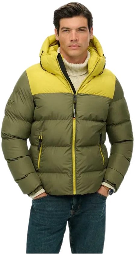 Model draagt een olijfgroene en gele gewatteerde jas met capuchon van Superdry, gecombineerd met een crèmekleurige trui.