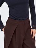 Detail van bruine wijde broek met plooien en donkerblauw shirt met kanten mouwboorden.