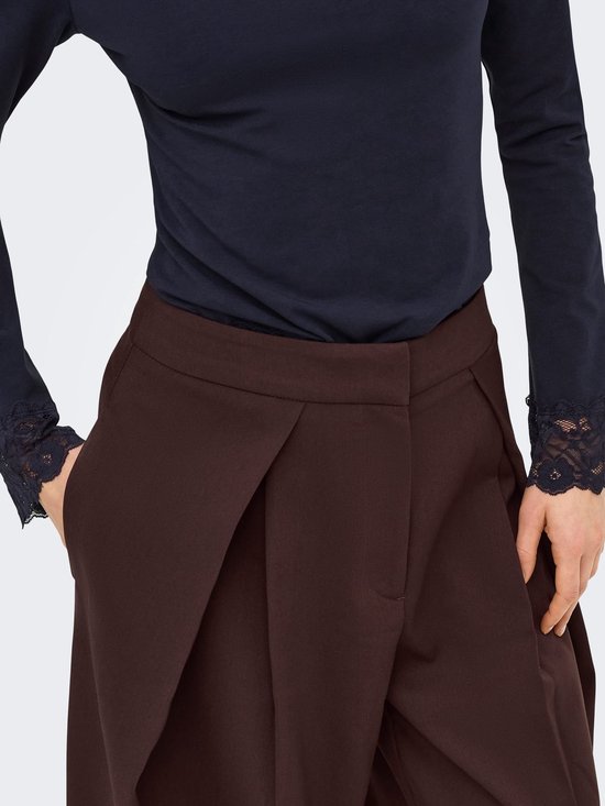 Detail van bruine wijde broek met plooien en donkerblauw shirt met kanten mouwboorden.