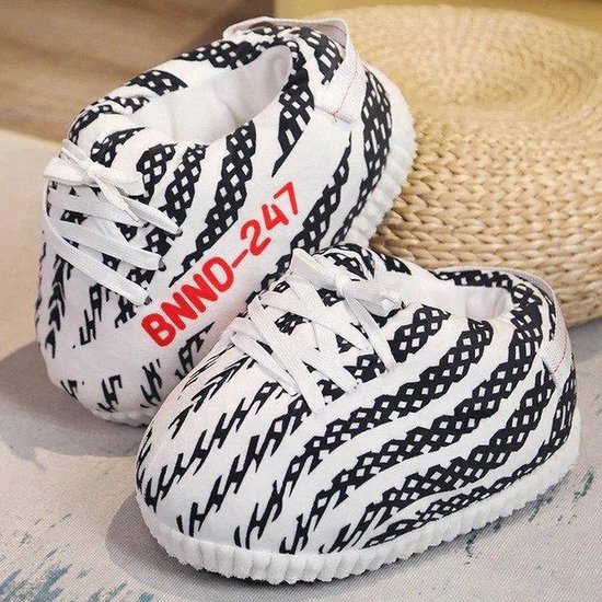 Zwart-witte sneaker-pantoffels met veters en rode BNND-247 tekst naast een rieten mand.