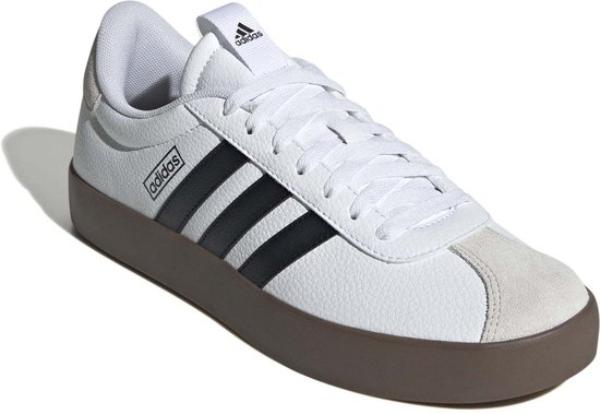 Witte Adidas sneakers met zwarte strepen, bruine zool en lichte schaduw.