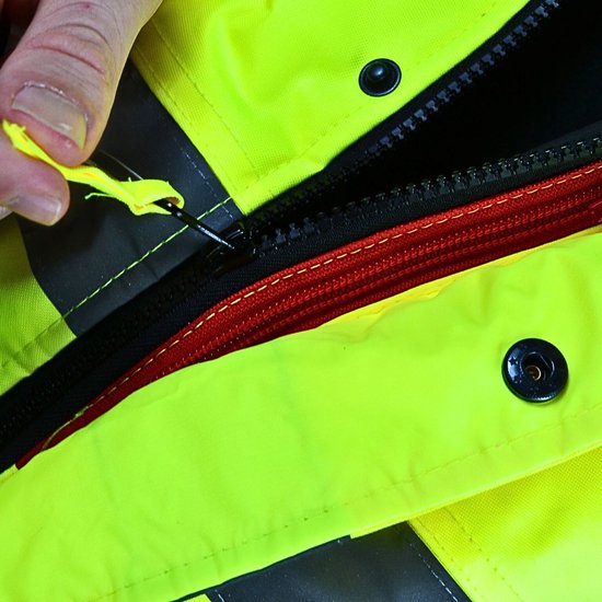 Buitenkant van een felgele jas, detail van de ritssluiting met rode bies. Een hand opent de rits.