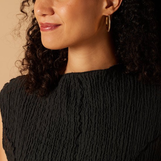 Model met grote, gouden hoepeloorbellen bezet met kristallen. Ze draagt een zwarte top.