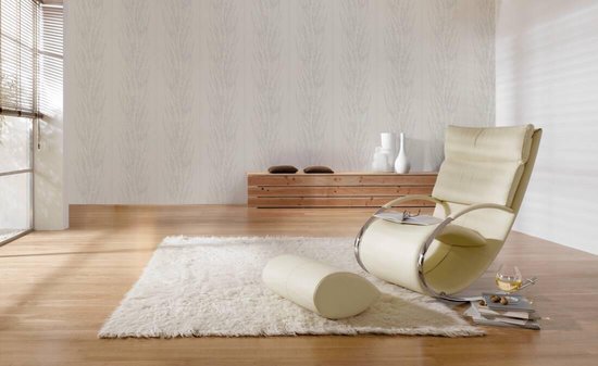 Een creme fauteuil staat op een donker houten vloer voor een muur met textielbehang met een verticaal dessin van takjes met bloesems.