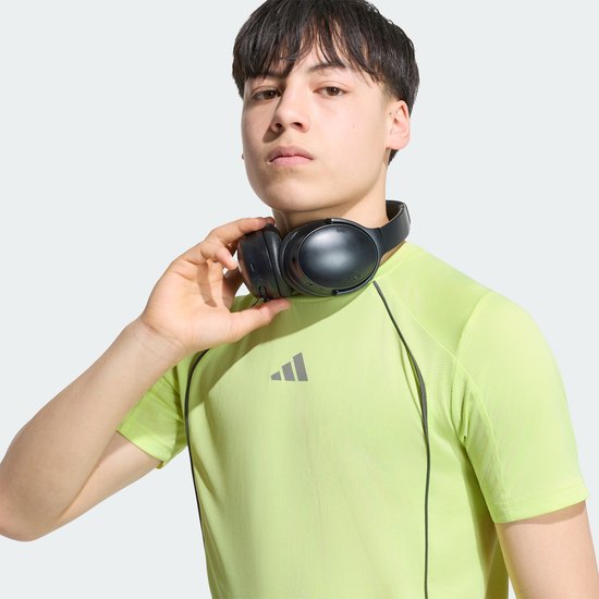 Jongen met koptelefoon om de nek, draagt geel T-shirt met korte mouwen en Adidas logo.