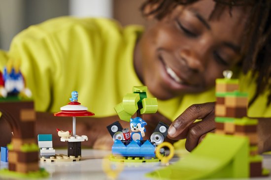 Een jongen met een gele trui die close-up met LEGO Sonic speelt, met Sonic op een platform met speakers.
