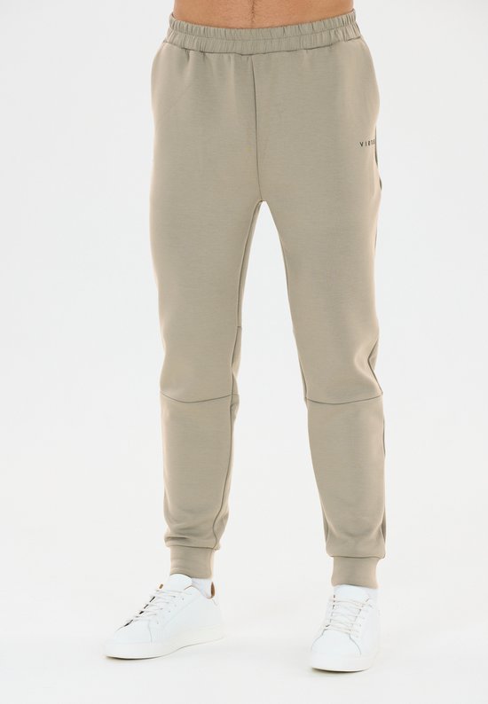Lichtbruine joggingbroek met elastische tailleband en witte sneakers, gedragen door een man.