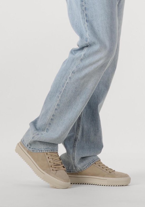 Model met crème suède lage sneakers met beige veters en lous lichtblauwe jeans.