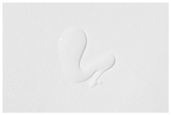 Een druppel heldere essence op een witte, getextureerde ondergrond.