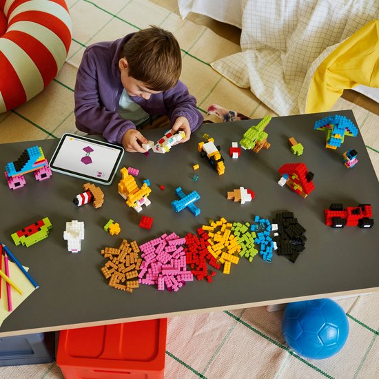 Een kind bouwt met LEGO op een tafel, met diverse creaties en losse stenen verspreid.