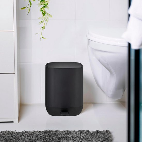 Zwarte pedaalemmer naast een toilet en witte kast in een badkamer.