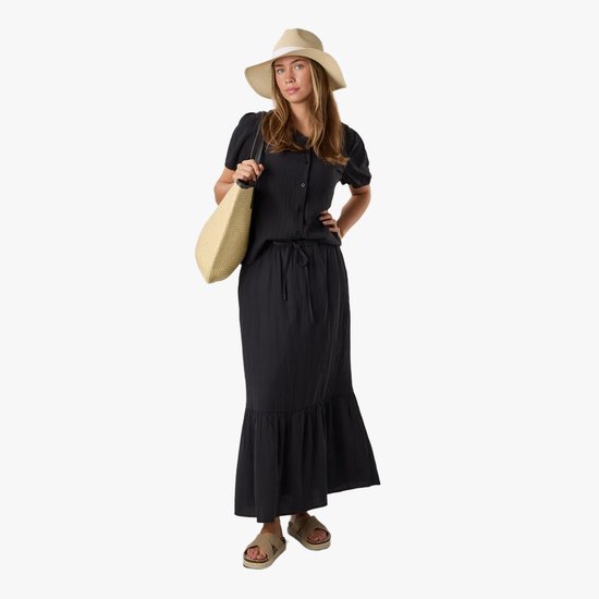 Model draagt zwarte crinkle lange rok met bijpassende blouse, strohoed en tas.