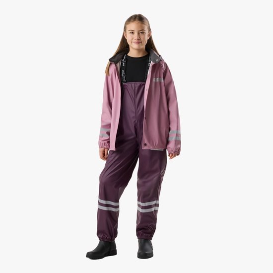 Meisje met lang bruin haar draagt een roze regenjas met paarse bretelbroek. Reflecterende strepen op jas en broek.
