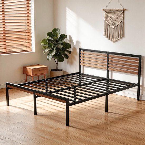 Bedframe van zwart metaal met houten hoofdbordlatten in een minimalistische slaapkamer met een kamerplant.