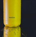 Gedetailleerde close-up van de gele en oranje ombre RVS drinkfles, bedekt met waterdruppels.