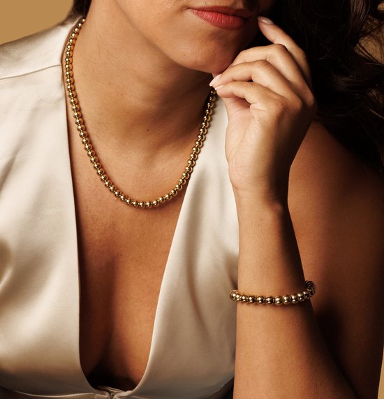 Close-up van een vrouw met gouden ketting met balletjes en bijpassende armband.