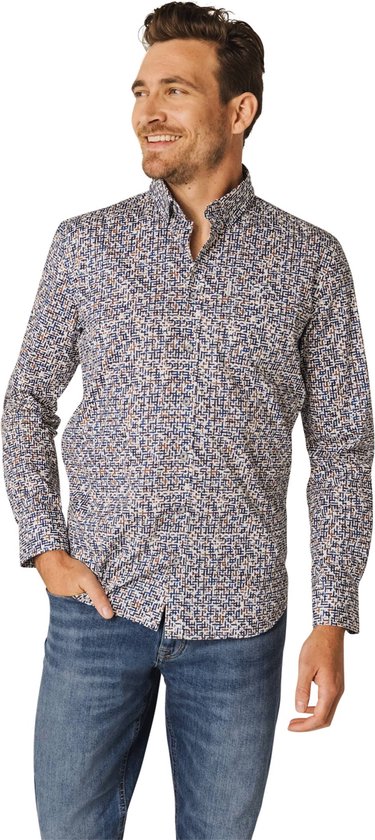 Man met hand in zijn broekzak draagt een blauw overhemd met een witte, bruine en donkerblauwe patroon. Hij draagt een jeans.
