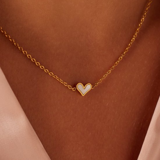 Gouden ketting met een klein wit hartje van parelmoer, dichtbij gedragen.