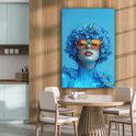 Portrait bleu d'une femme avec des lunettes orange et des fleurs, dans une cuisine-salle à manger.