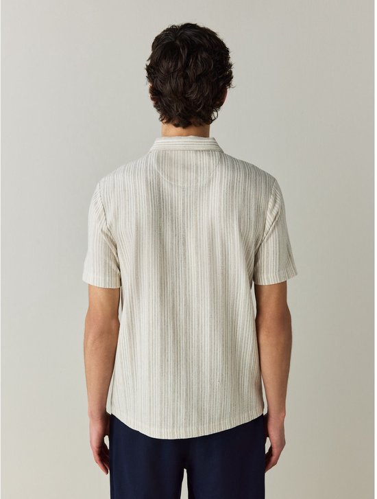 Achterkant van een man in een beige polo met fijne verticale strepen, gedragen met een marineblauwe broek.