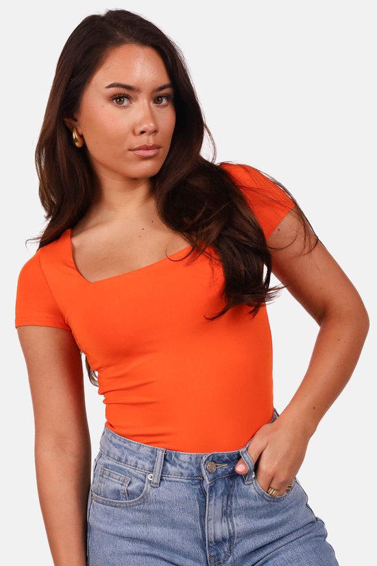 Model met oranje T-shirt met vierkante hals en spijkerbroek.