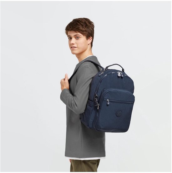Homme portant un sac à dos Kipling bleu foncé sur le dos, vêtu d'une veste grise.