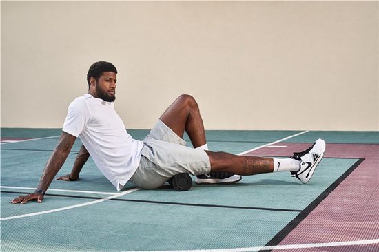 Basketbalspeler Paul George gebruikt een zwarte schuimroller op zijn been op een sportveld.
