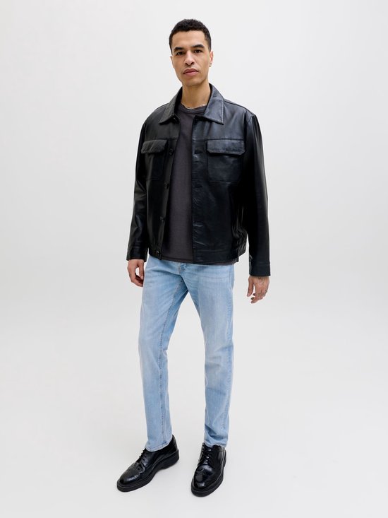 Model in zwart leren jack, grijs t-shirt en lichtblauwe slim fit jeans, volledig zicht.