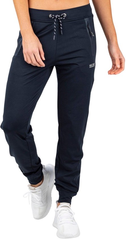 Vrouw in donkerblauwe sportbroek met trekkoord, ritssluitingen en witte sneakers.
