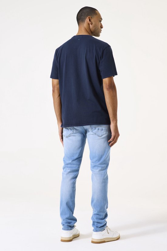 Man met donkere huid in een donkerblauw T-shirt en lichtblauwe spijkerbroek, gezien vanaf de achterkant.