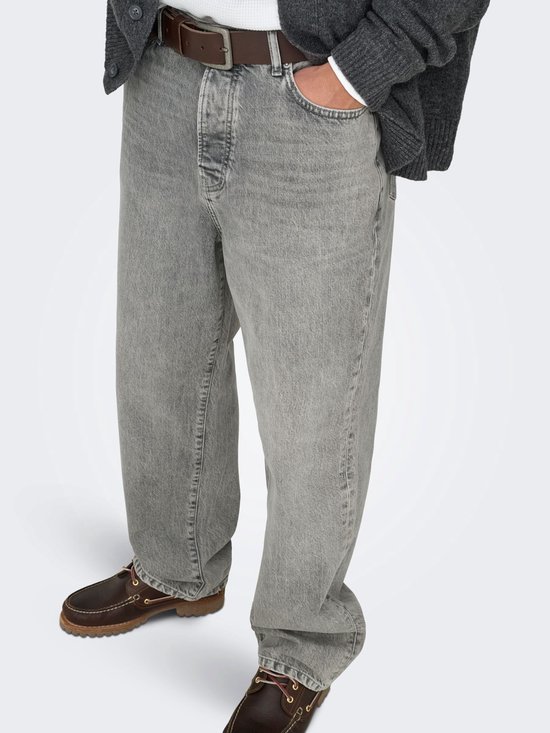 Een man draagt een grijze jeans met rechte pijpen, een bruine riem en bruine instappers.