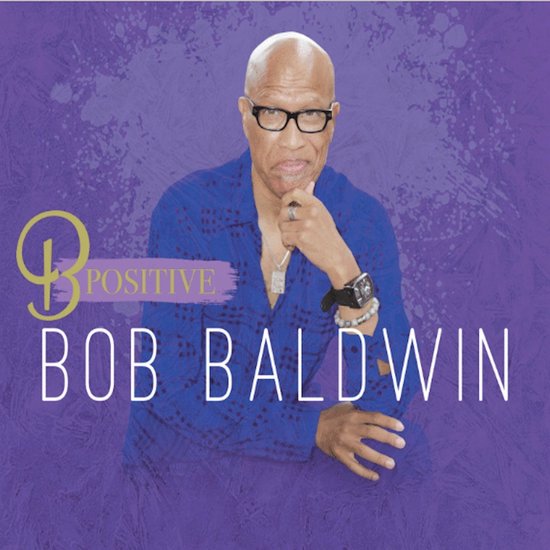 Bob Baldwin in een blauw shirt met bril tegen een paarse achtergrond, met de tekst 'B Positive' en zijn naam.