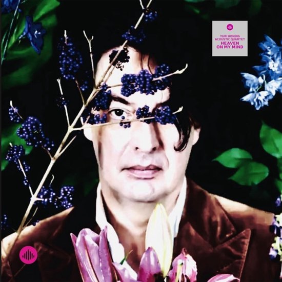 Albumhoes 'Heaven On My Mind' van Yuri Honing Acoustic Quartet. Close-up van een man met donkere krullen, bruine jas, omringd door paarse en blauwe bloemen en donkere bessen.