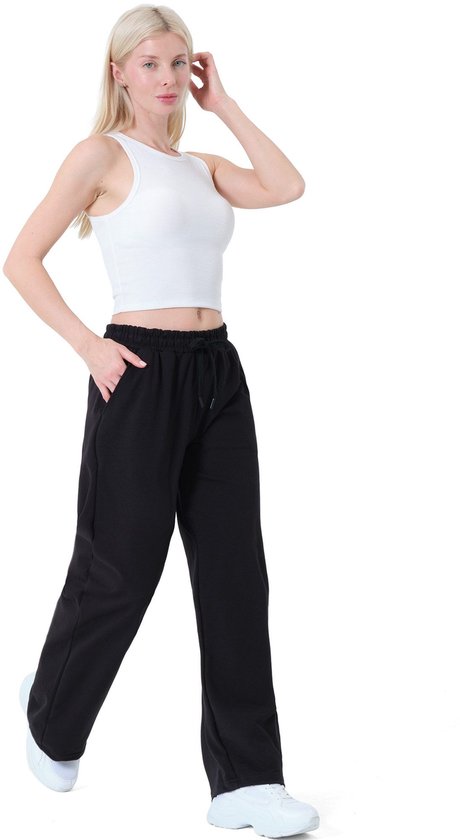 Model loopt in een zwarte wijde joggingbroek met trekkoord en witte tanktop.