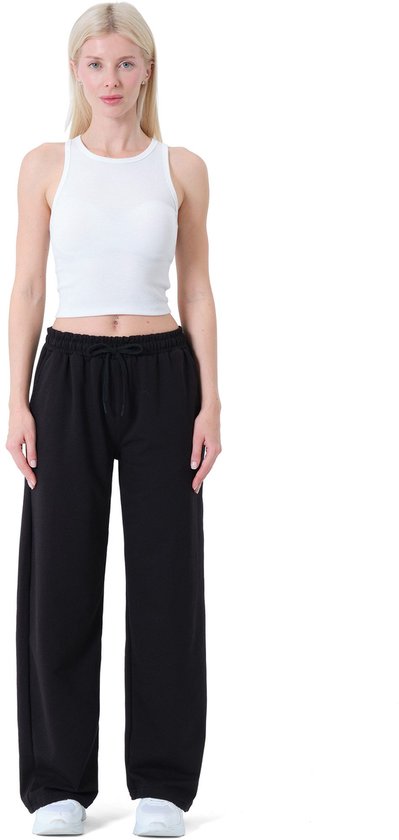 Model draagt een zwarte wijde joggingbroek met trekkoord en witte tanktop.