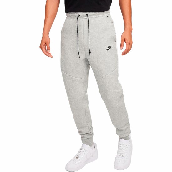 Man in een grijze Nike joggingbroek met een zwarte ritszak op de zijkant.