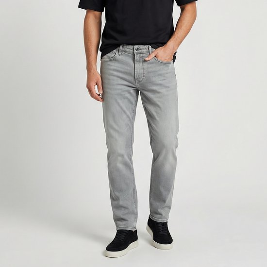 Man in een lichtgrijze jeans en een zwarte T-shirt. Zwarte sneakers.
