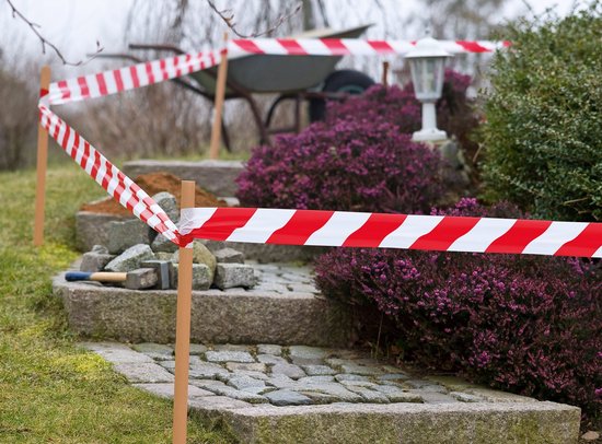 Rood-wit waarschuwingslint om een tuinpad met stenen trap en struiken.