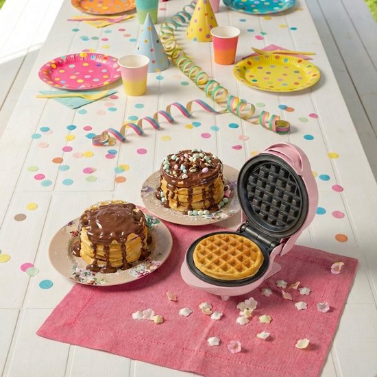 Roze mini wafelijzer op een feestelijk gedekte tafel met pannenkoeken en confettie.