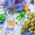 Verres Duralex Manhattan verts et transparents avec boissons, raisins et confettis.