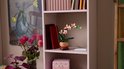 LEGO orchidee in een pot op een boekenplank, naast boeken en een vaas met bloemen.