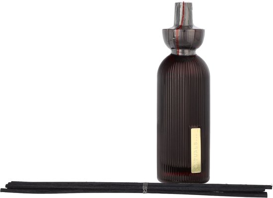 Donkere glazen diffuser met ribbelpatroon en gouden etiket, naast zwarte geurstokjes.