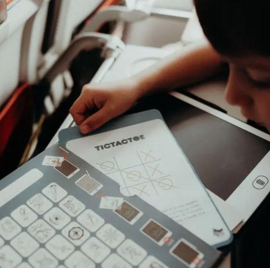 Kind in vliegtuigstoel, spelend met TicTacToe kaart en tablet.