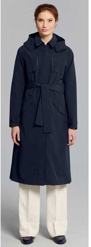 Vrouw in lange donkerblauwe jas met capuchon, ceintuur en witte broek, van voren gezien.