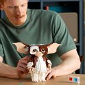 Een man met rood haar kijkt naar een LEGO Ideas Gizmo figuur die hij in handen heeft. Het figuur is bruin-wit en heeft grote oren.