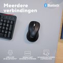 Zwarte Trust muis op een muismat naast een toetsenbord, met Bluetooth-logo.