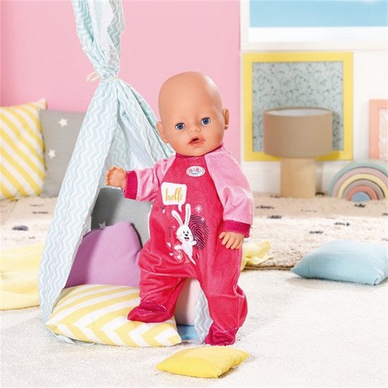 Baby pop in roze pyjama met konijnprint en 'hello' tekst, staand bij een tipi.