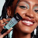 Model met donkere vlechten en turquoise oogschaduw houdt een transparante e.l.f. Power Grip Primer vast.